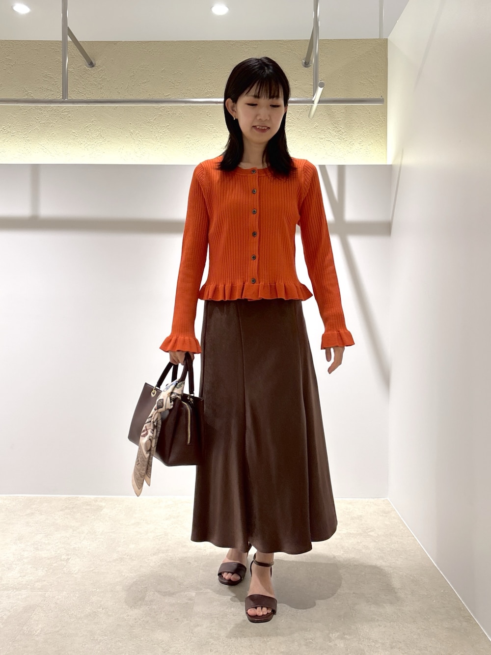 オレンジ系のニット/セーター、ブラウン系のスカート、レッド系のトートバッグを着用したレディースの夏コーディネートの1枚目の写真