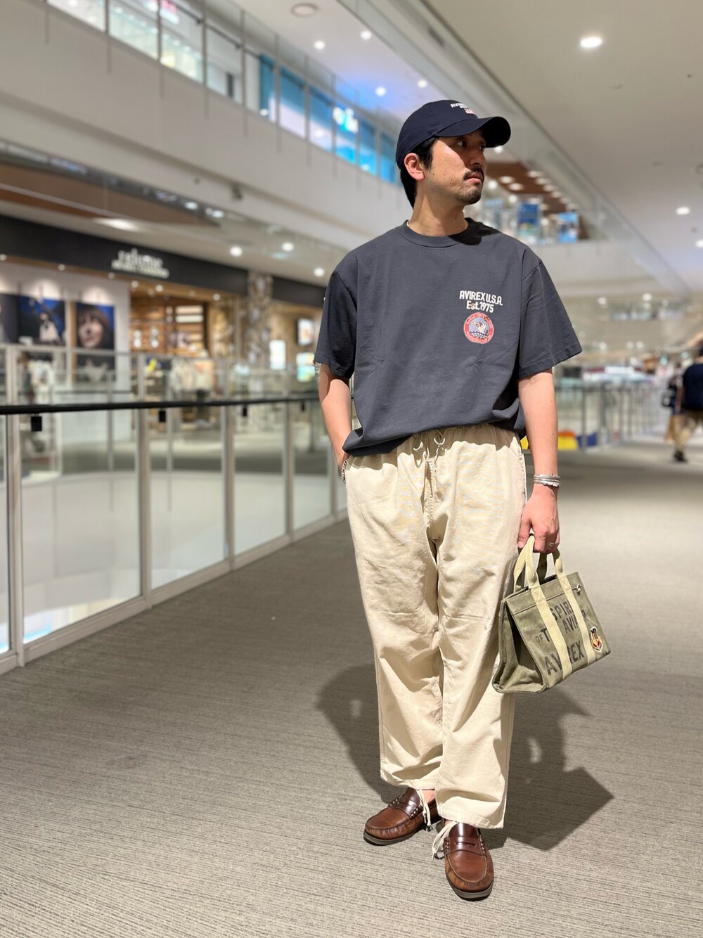 ブラック系のTシャツ/カットソー、ベージュ系のカーゴパンツ、グリーン系のトートバッグを着用したメンズの春コーディネートの1枚目の写真