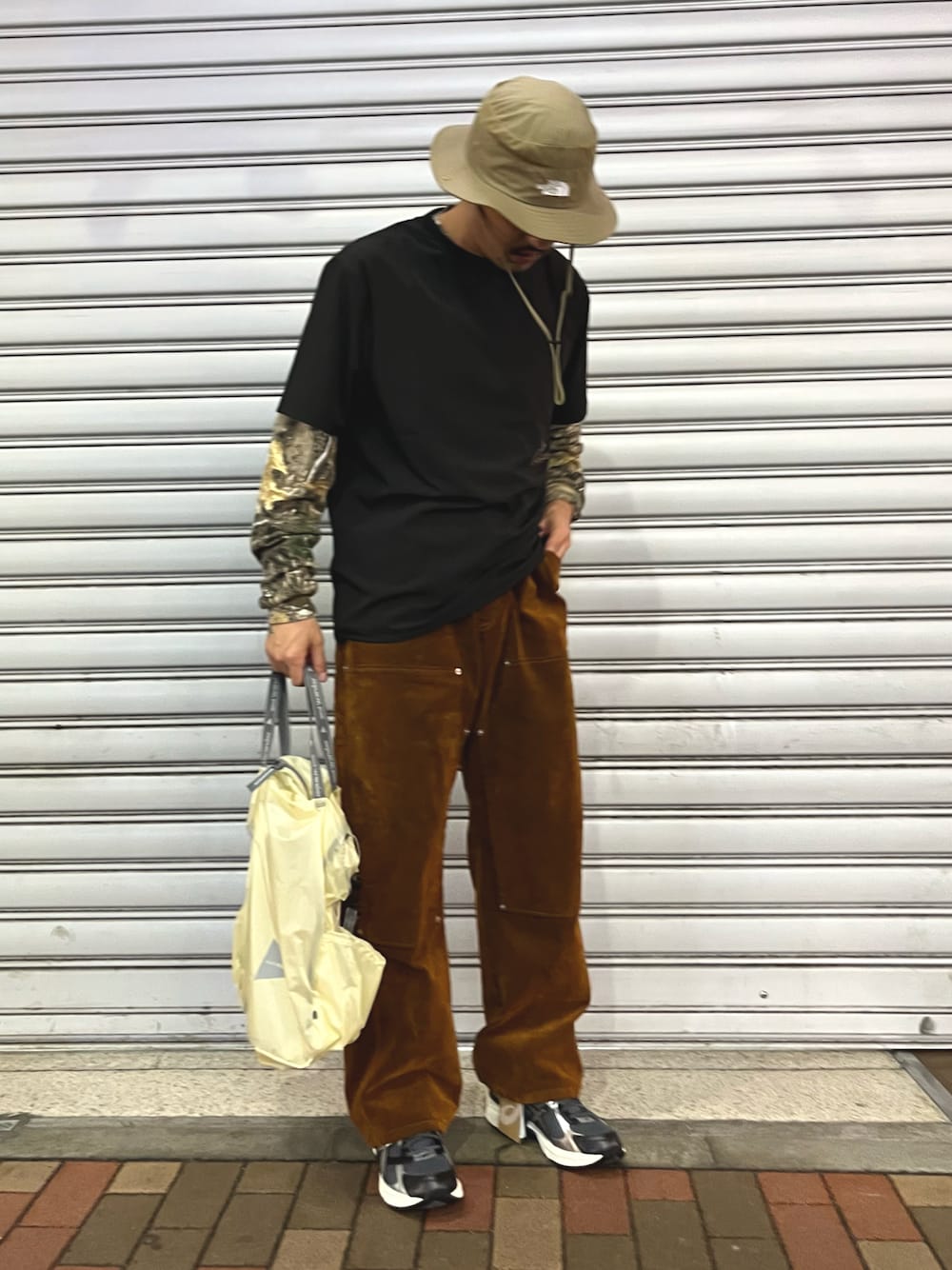 ブラウン系のデニムパンツ、ホワイト系のトートバッグ、ブラック系のTシャツ/カットソーを着用したメンズの秋コーディネートの1枚目の写真