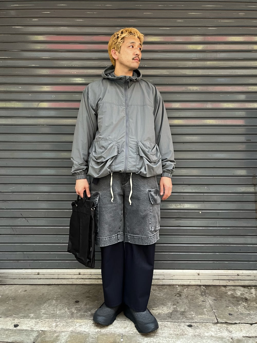 グレー系のパンツ、ブラック系のショルダーバッグ、ブラック系のスリッポンを着用したメンズの春コーディネートの1枚目の写真