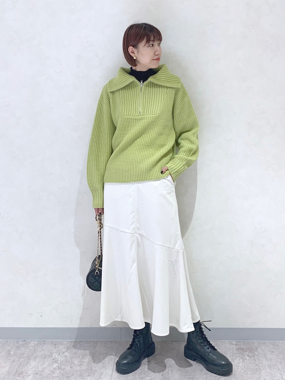 イエロー系のニット/セーター、ホワイト系のスカート、ブラック系のブーツを着用したレディースの秋コーディネートの1枚目の写真