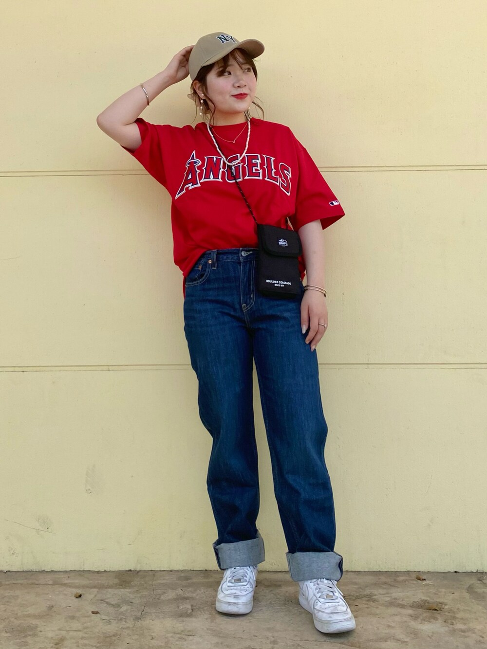 レッド系のTシャツ/カットソー、ブラック系のショルダーバッグ、ブルー系のデニムパンツを着用したレディースの春コーディネートの1枚目の写真