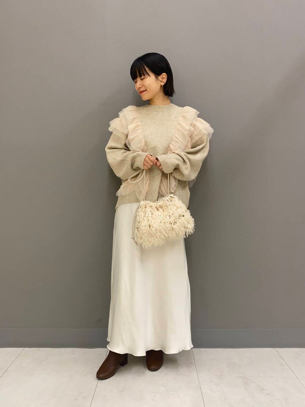 イエロー系のブーツ、ホワイト系のハンドバッグ、ホワイト系のスカートを着用したレディースの秋コーディネートの1枚目の写真