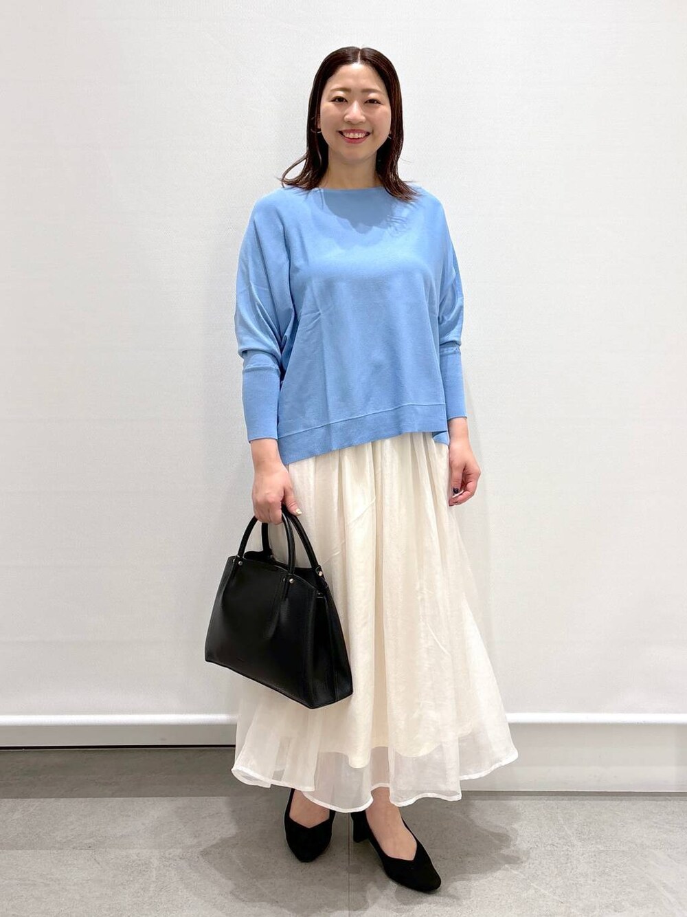 ホワイト系のスカート、ブラック系のショルダーバッグ、ブラック系のパンプスを着用したレディースの春コーディネートの1枚目の写真