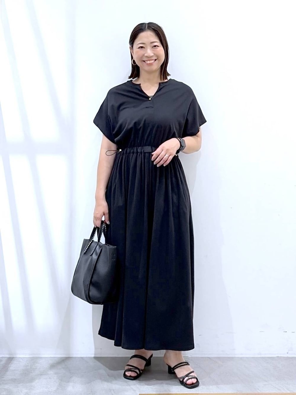 ブラック系のワンピース、ブラック系のサンダル、ブラック系のトートバッグを着用したレディースの夏コーディネートの1枚目の写真