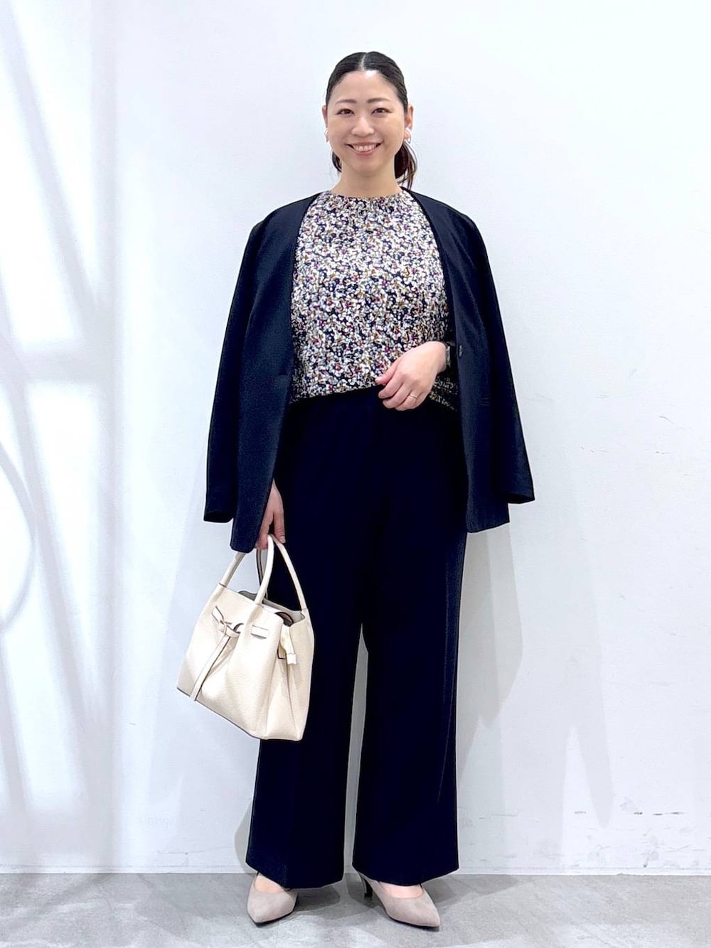 ベージュ系のパンプス、ベージュ系のハンドバッグ、ブルー系のノーカラージャケットを着用したレディースの春コーディネートの1枚目の写真