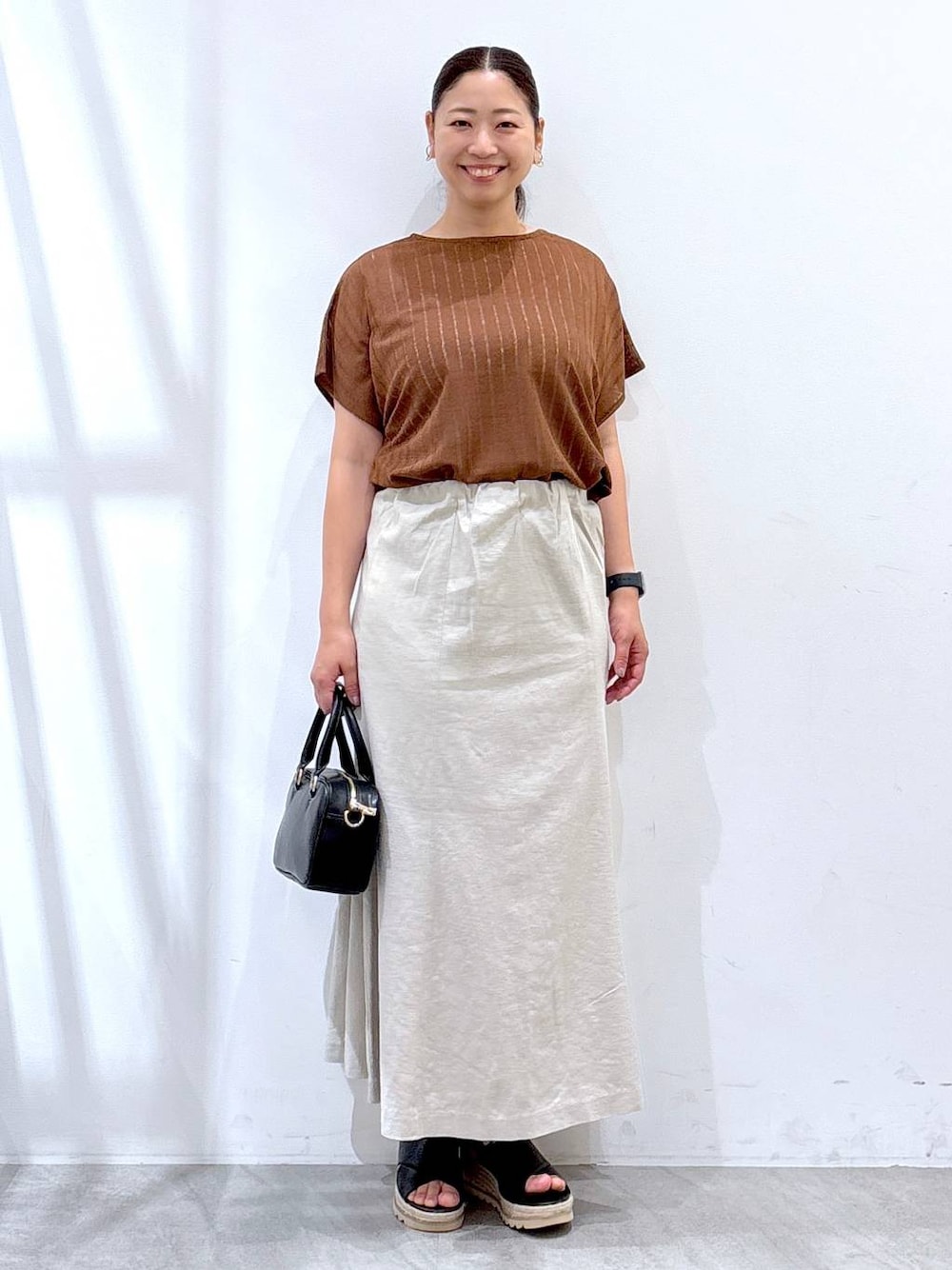 ベージュ系のスカート、ブラック系のハンドバッグ、ブラウン系のTシャツ/カットソーを着用したレディースの夏コーディネートの1枚目の写真