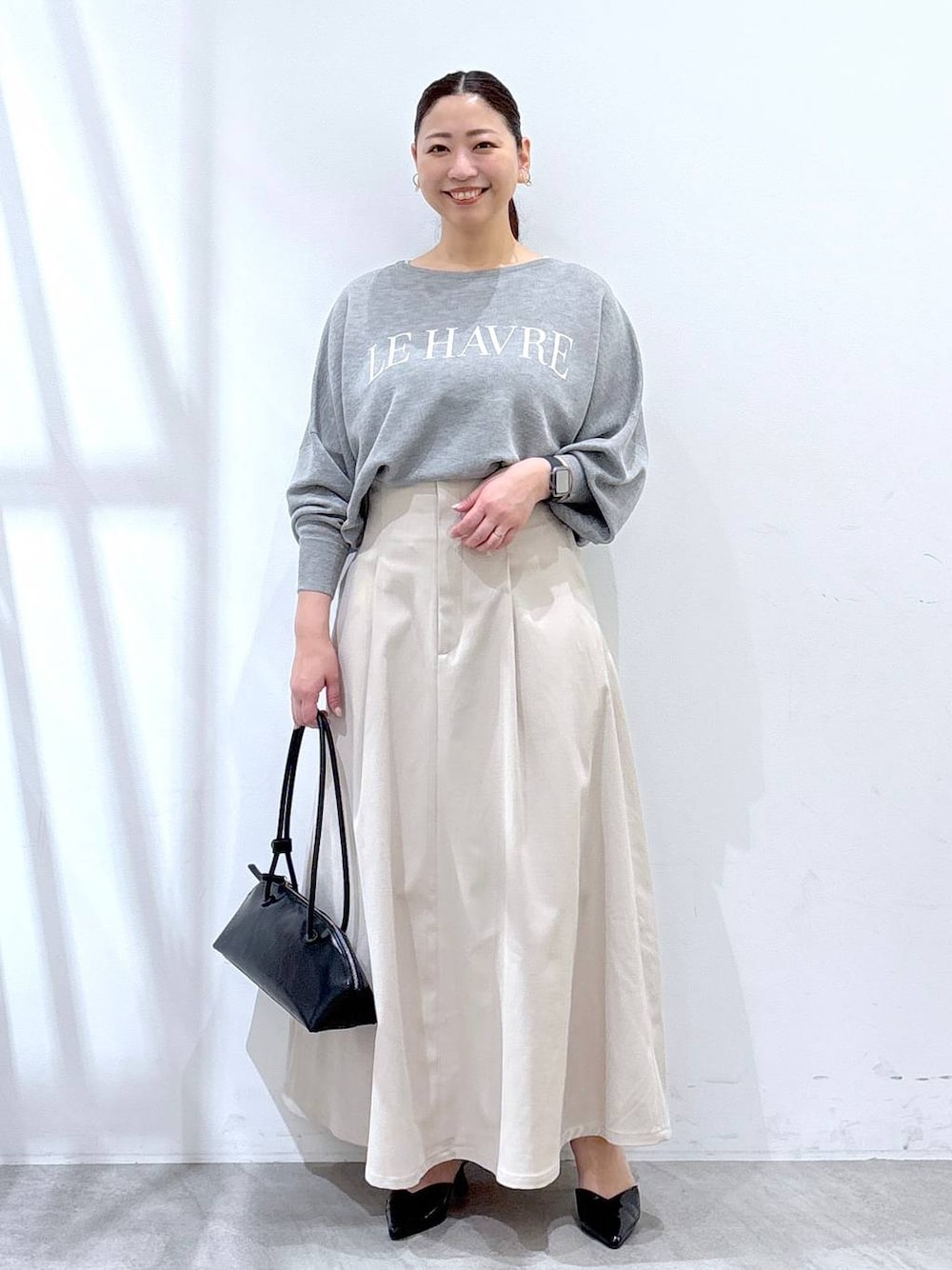 ブラック系のハンドバッグ、グレー系のニット/セーター、ベージュ系のスカートを着用したレディースの春コーディネートの1枚目の写真