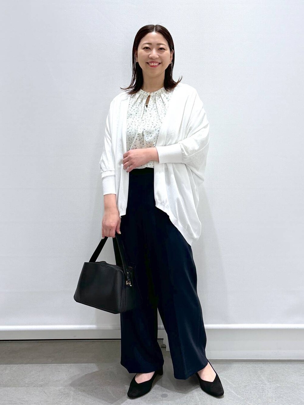 イエロー系のシャツ/ブラウス、ホワイト系のカーディガン/ボレロ、ブラック系のハンドバッグを着用したレディースの春コーディネートの1枚目の写真