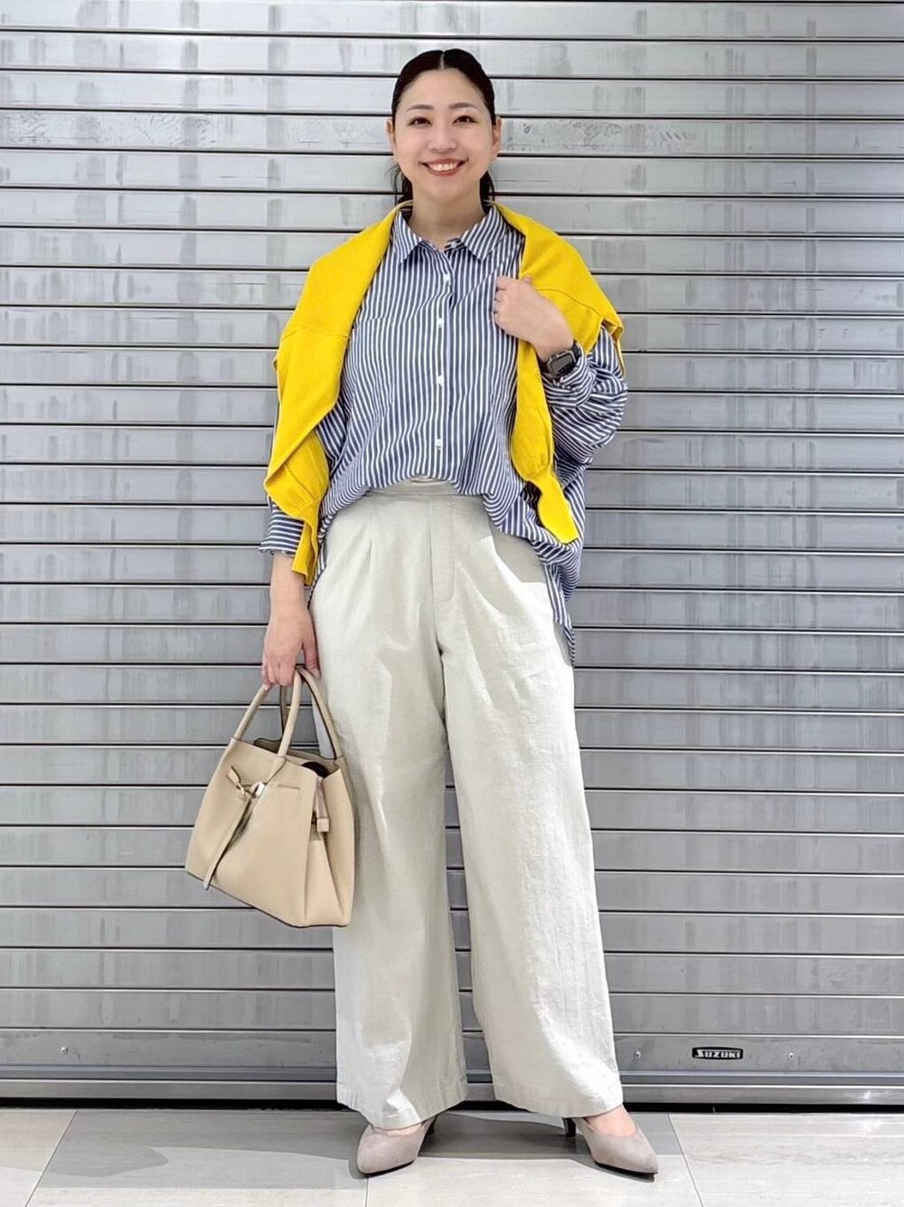 ベージュ系のパンプス、ベージュ系のハンドバッグ、イエロー系のニット/セーターを着用したレディースの春コーディネートの1枚目の写真