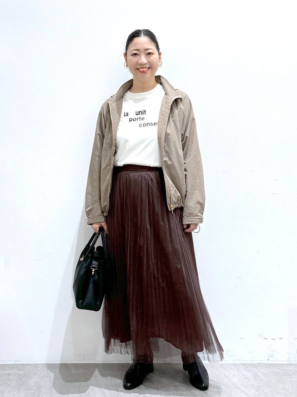 ブラック系のハンドバッグ、ブラウン系のスカート、ホワイト系のTシャツ/カットソーを着用したレディースの秋コーディネートの1枚目の写真
