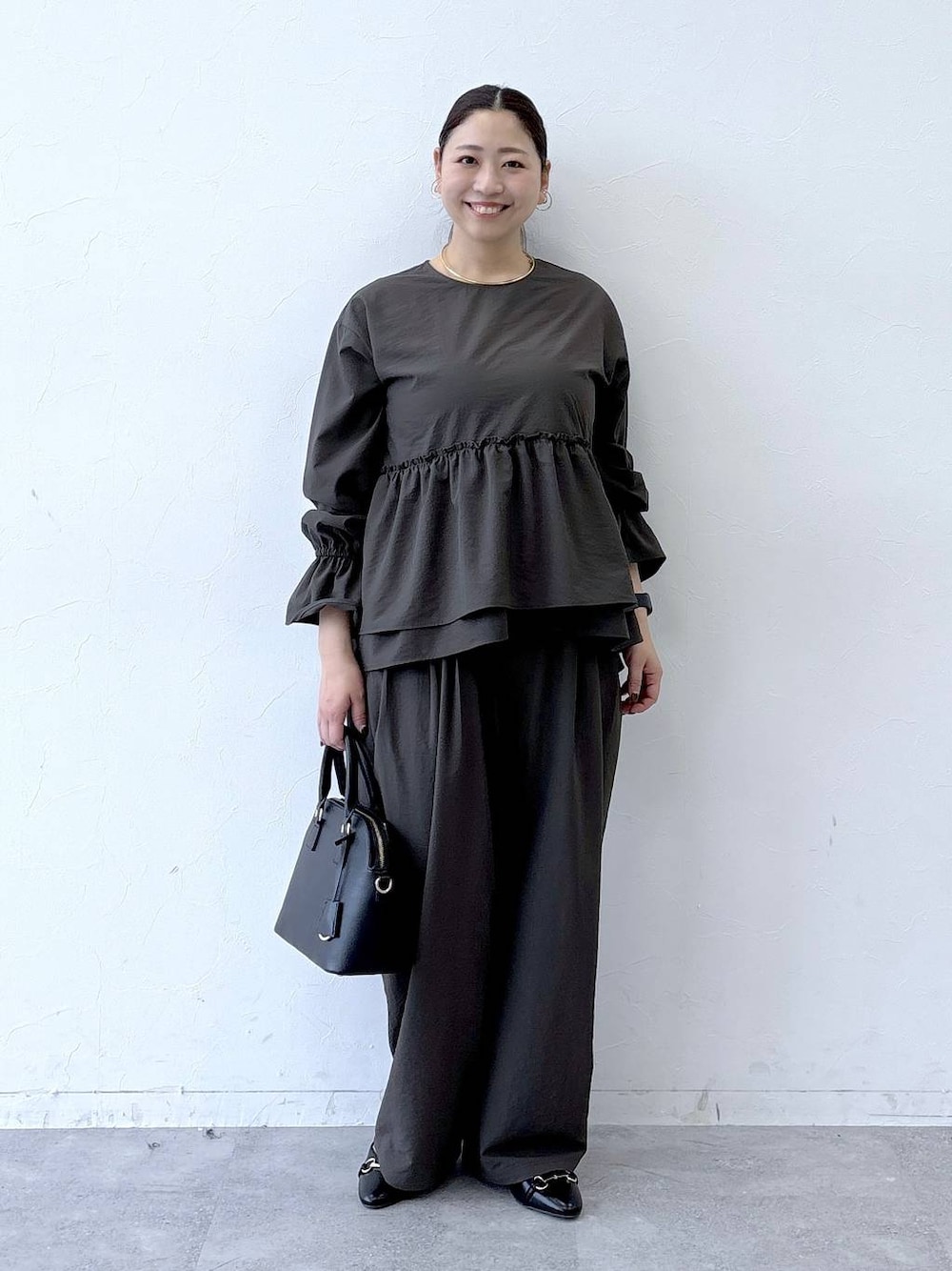 ブラック系のハンドバッグ、ブラック系のパンプス、ブラウン系のその他パンツを着用したレディースの冬コーディネートの1枚目の写真