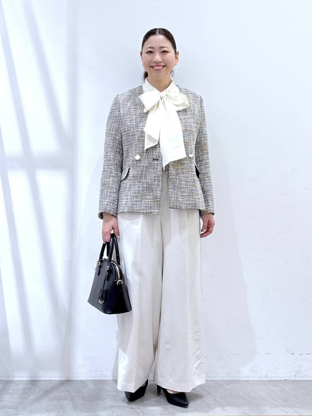 ブラック系のハンドバッグ、ブラック系のノーカラージャケット、ホワイト系のシャツ/ブラウスを着用したレディースの冬コーディネートの1枚目の写真