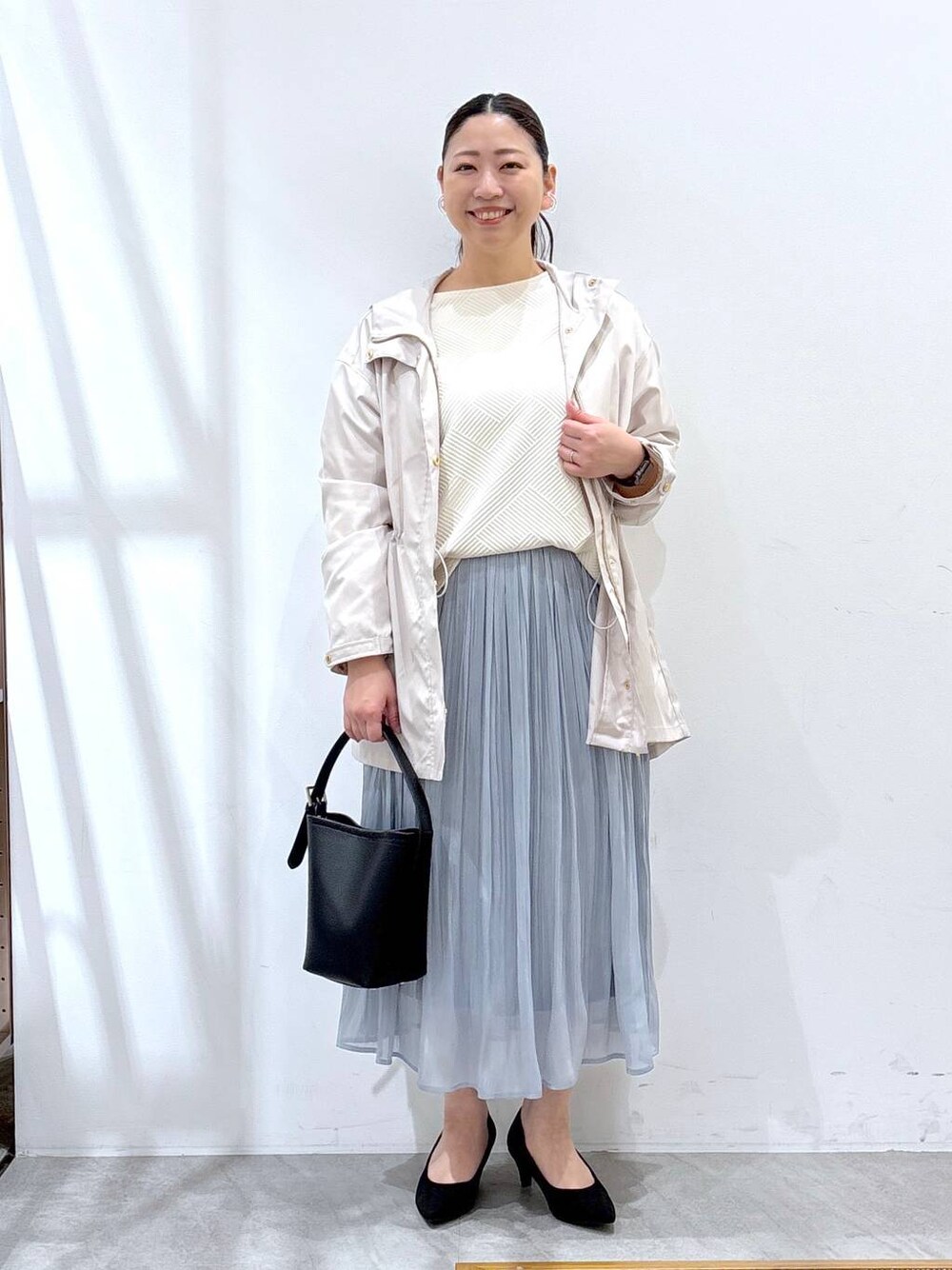 ブラック系のパンプス、ブルー系のスカート、ブラック系のハンドバッグを着用したレディースの春コーディネートの1枚目の写真