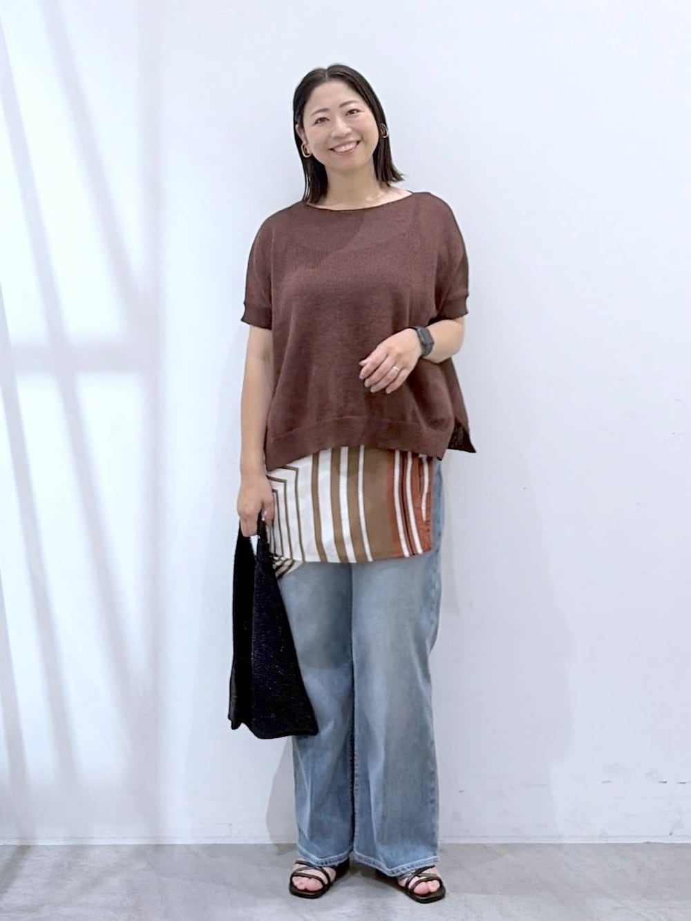 ブラック系のサンダル、ブルー系のデニムパンツ、ブラウン系のストール/ショールを着用したレディースの秋コーディネートの1枚目の写真