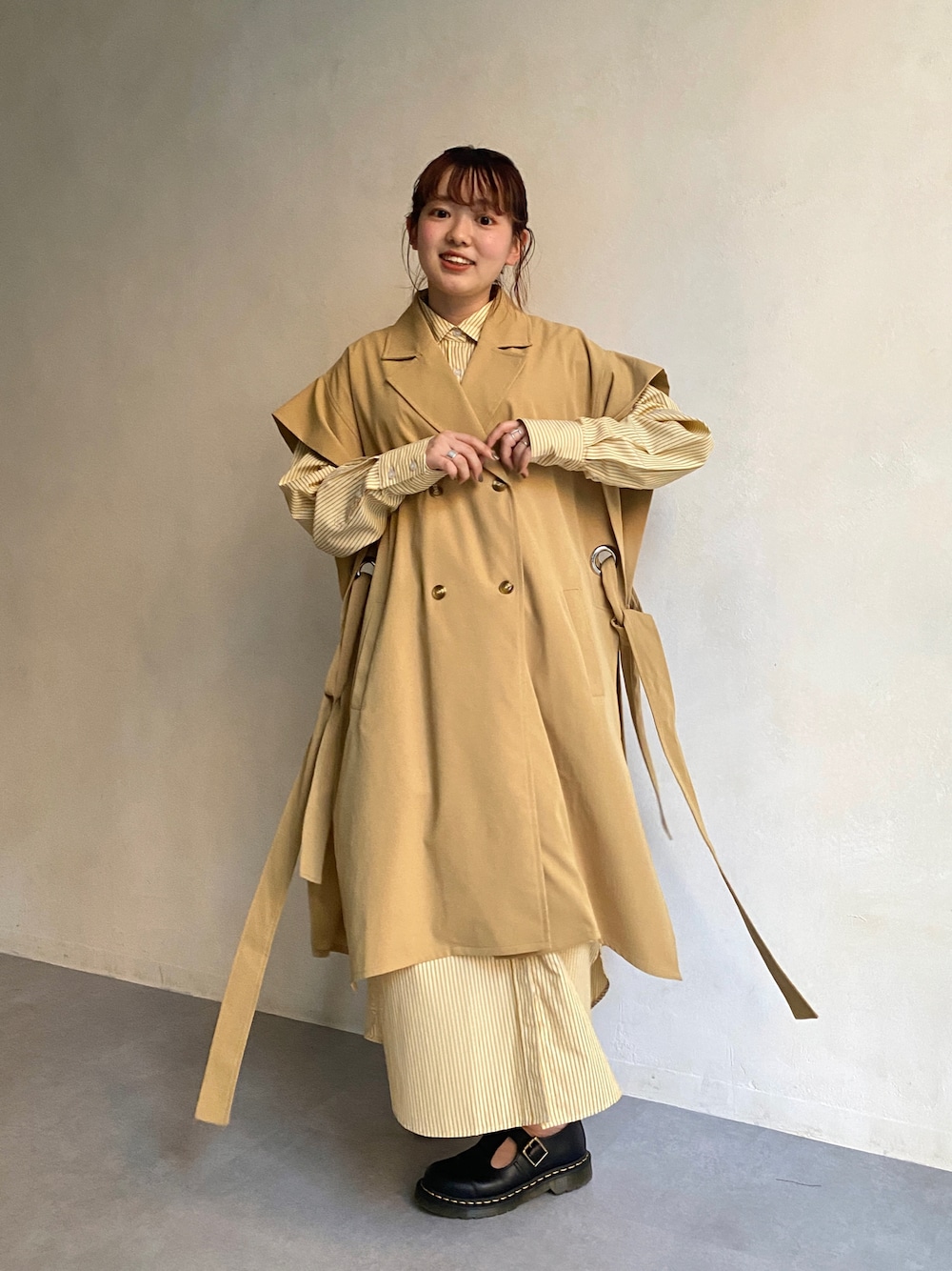 ベージュ系のトレンチコート、イエロー系のシャツワンピース、ブラック系のローファーを着用したレディースの冬コーディネートの1枚目の写真