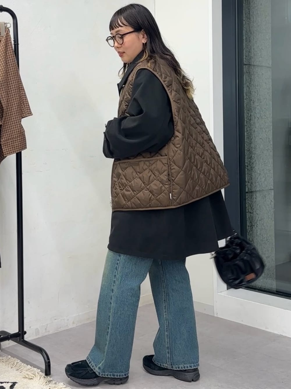 ブラック系のその他アウター、ブラック系のショルダーバッグ、ブルー系のデニムパンツを着用したレディースの秋コーディネートの1枚目の写真