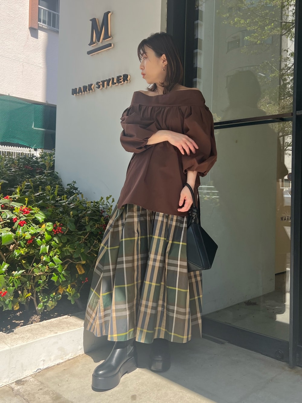 グリーン系のスカート、ブラウン系のシャツ/ブラウス、ブラック系のハンドバッグを着用したレディースの春コーディネートの1枚目の写真