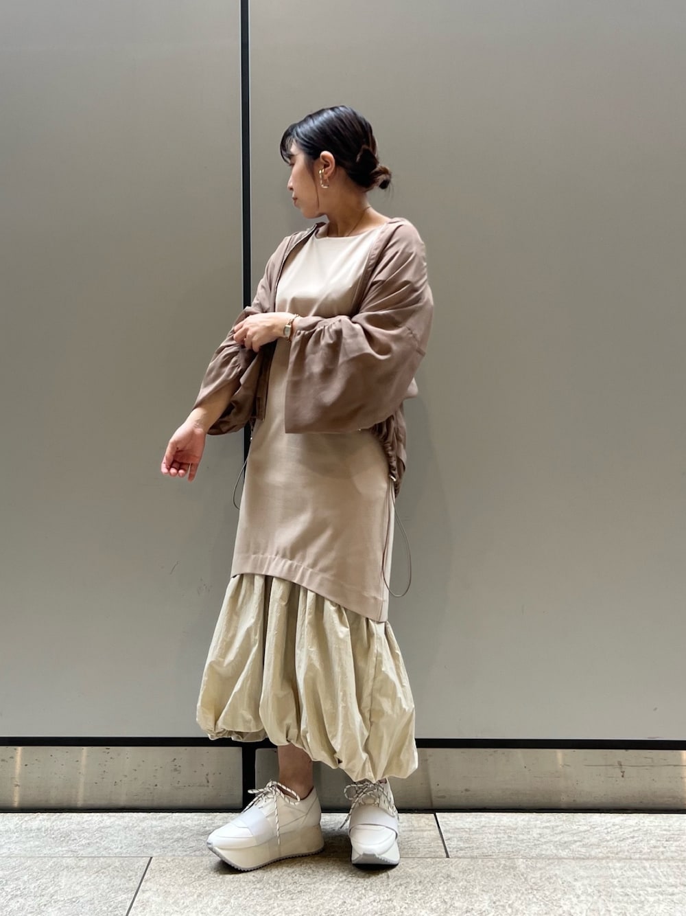 ベージュ系のワンピース、ホワイト系のスニーカー、ブラウン系のブルゾンを着用したレディースの春コーディネートの1枚目の写真