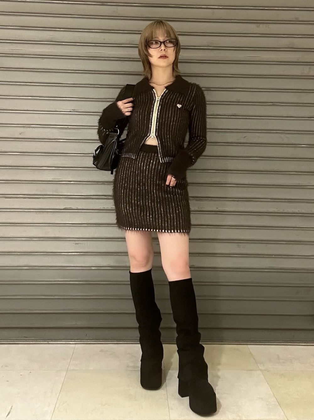 ブラウン系のニット/セーター、ブラウン系のスカート、ブラック系のブーツを着用したレディースの秋コーディネートの1枚目の写真