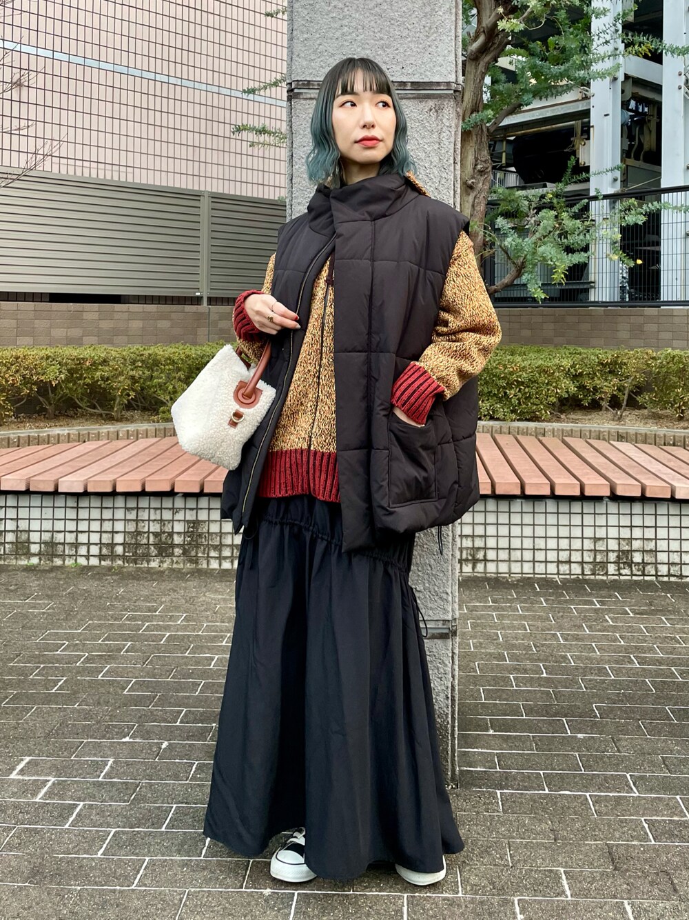 ブラック系のベスト、オレンジ系のパーカー、ブラック系のスカートを着用したレディースの冬コーディネートの1枚目の写真