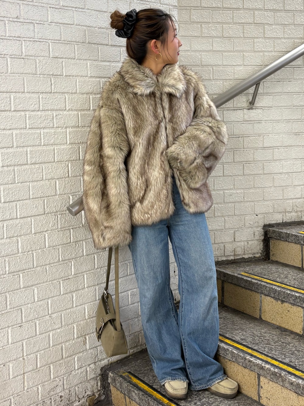 ベージュ系のダウンジャケット/コート、グリーン系のハンドバッグ、ブルー系のデニムパンツを着用したレディースの秋コーディネートの1枚目の写真