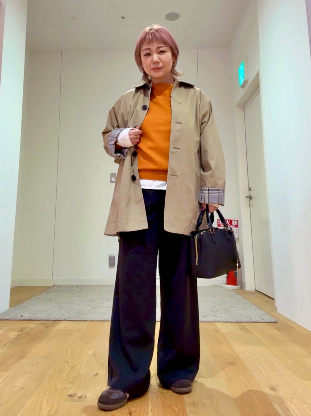 ブラック系のハンドバッグ、ホワイト系のTシャツ/カットソー、ベージュ系のステンカラーコートを着用したレディースの秋コーディネートの1枚目の写真