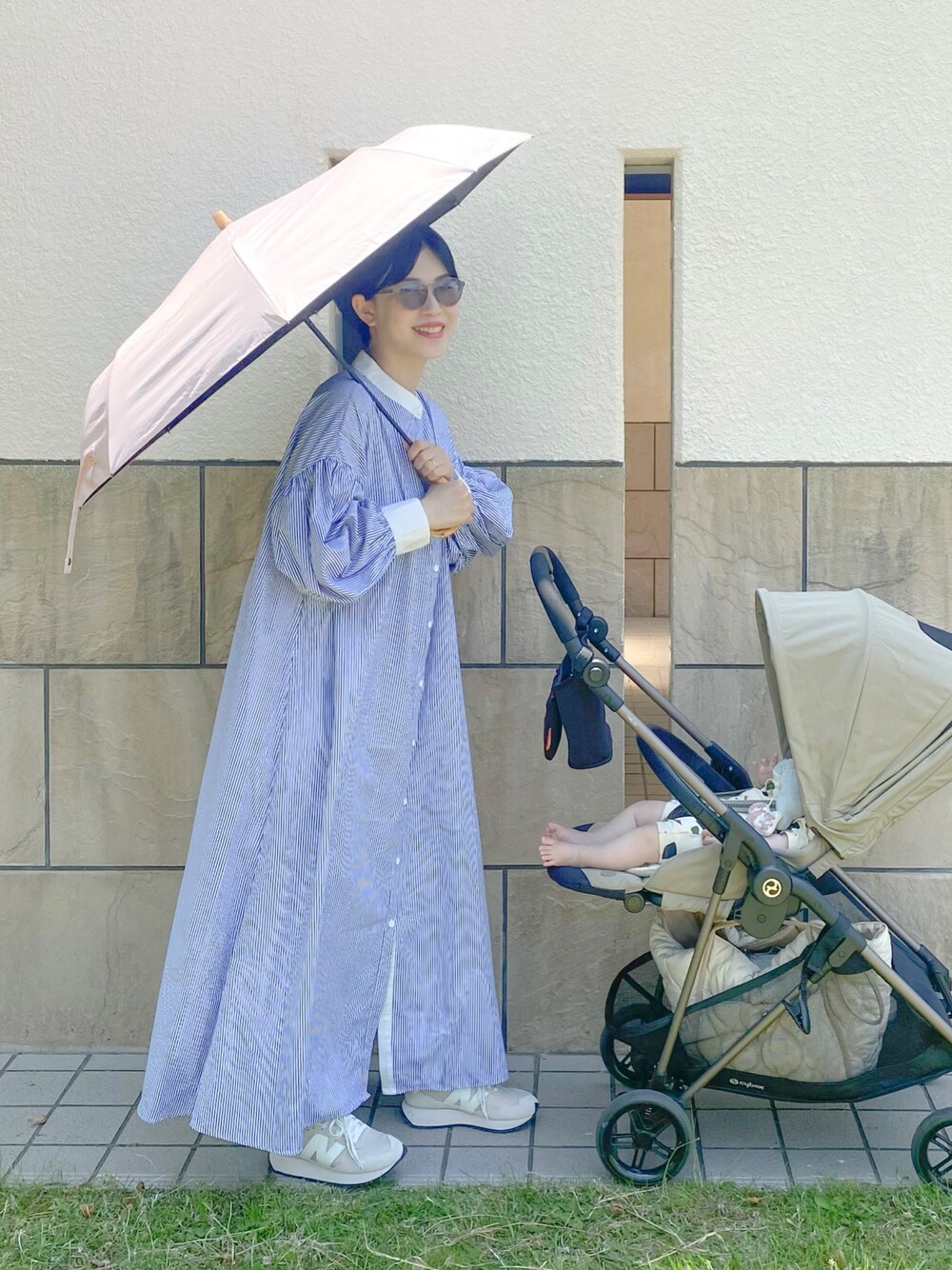 ブルー系のワンピース、ホワイト系のスニーカー、ピンク系の折りたたみ傘を着用したレディースの春コーディネートの1枚目の写真