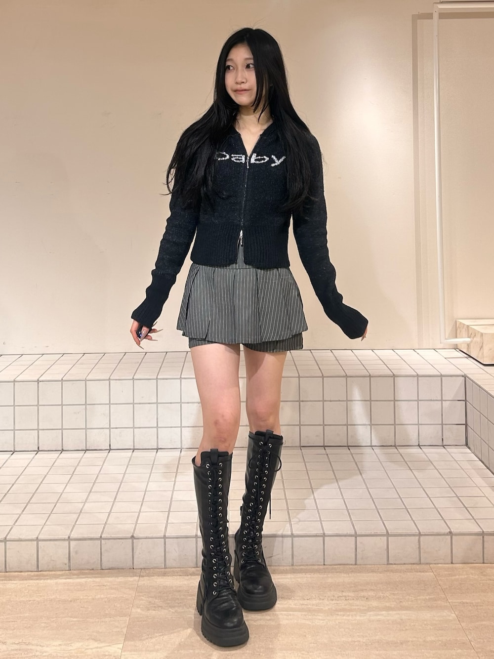 ブラック系のパーカー、グレー系のスカート、ブラック系のブーツを着用したレディースの冬コーディネートの1枚目の写真