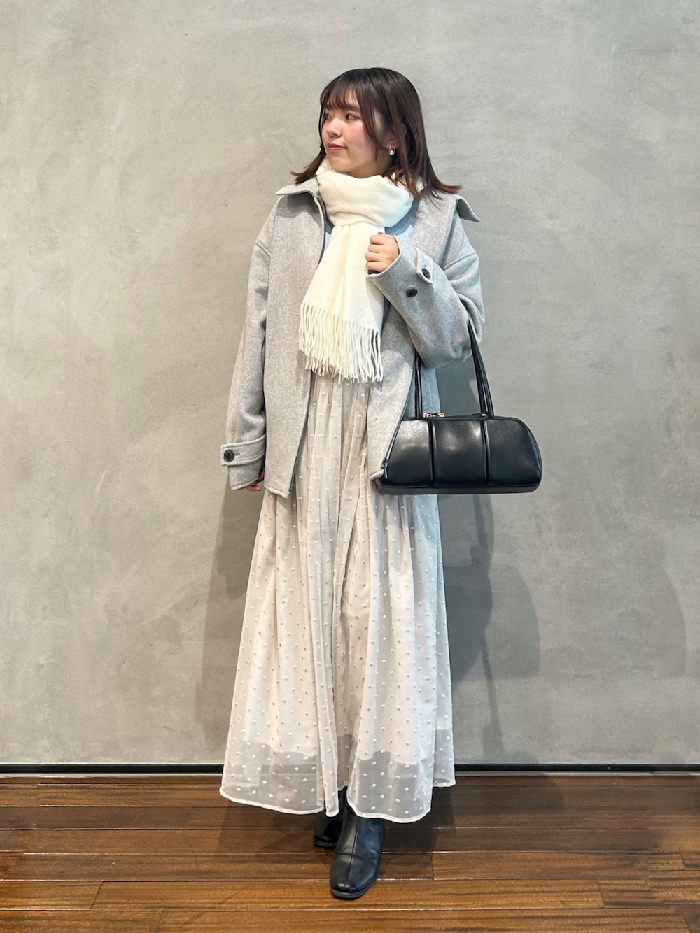 グレー系のステンカラーコート、ブルー系のカーディガン/ボレロ、ホワイト系のスカートを着用したレディースの冬コーディネートの1枚目の写真