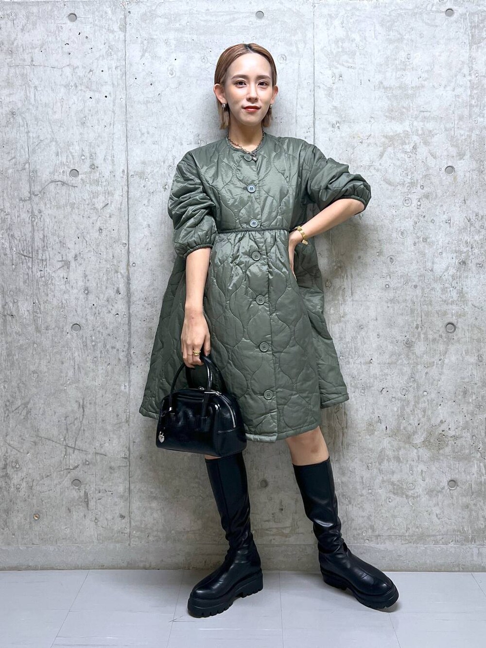 グリーン系のミリタリージャケット、ブラック系のブーツ、ブラック系のボストンバッグを着用したレディースの秋コーディネートの1枚目の写真