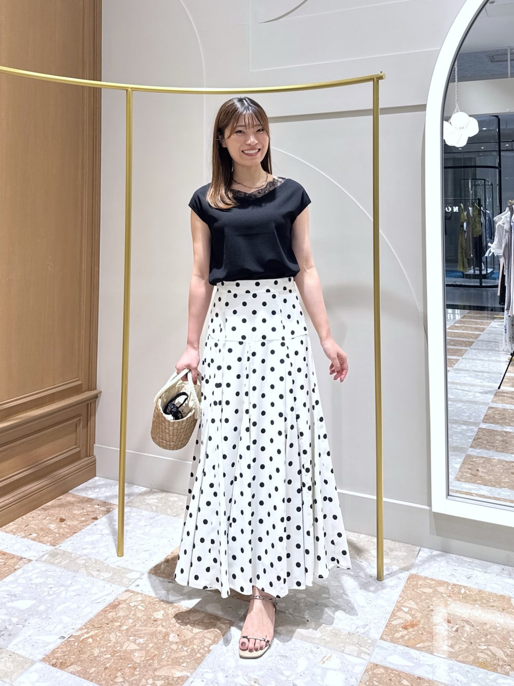 ブラック系のニット/セーター、ホワイト系のスカート、ベージュ系のかごバッグを着用したレディースの夏コーディネートの1枚目の写真