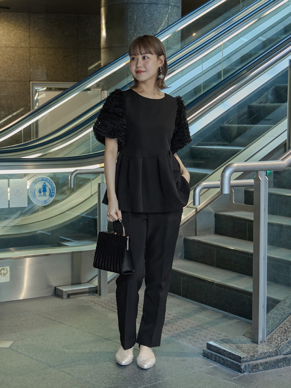 ブラック系のスーツセット、ブラック系のハンドバッグ、ベージュ系のパンプスを着用したレディースの秋コーディネートの1枚目の写真