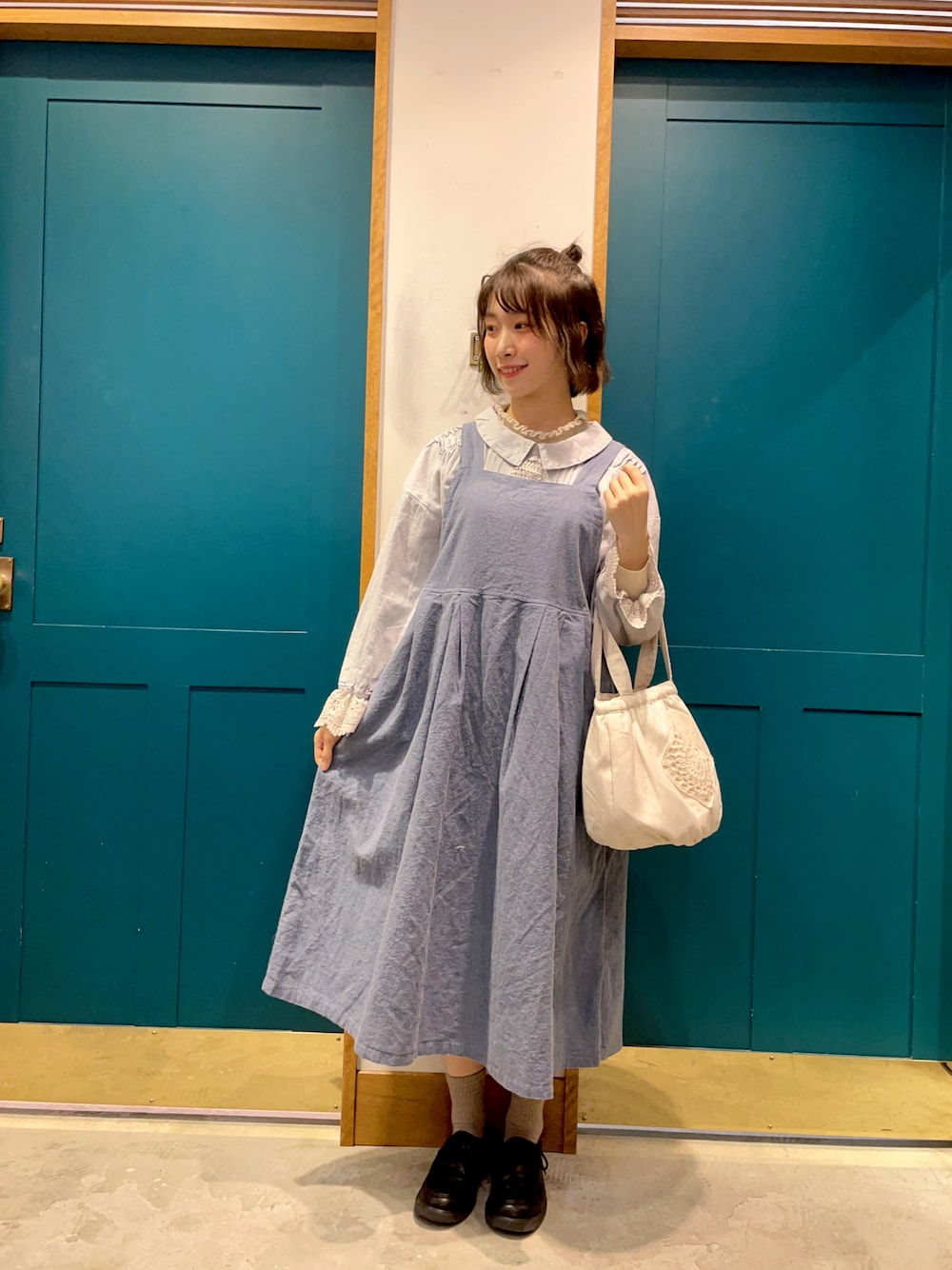 ブルー系のシャツ/ブラウス、ブルー系のジャンパースカート、ホワイト系のトートバッグを着用したレディースの冬コーディネートの1枚目の写真