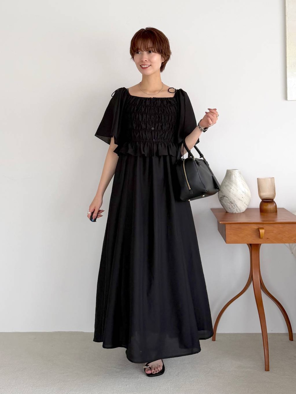 ブラック系のワンピース、ブラック系のハンドバッグ、ブラック系のサンダルを着用したレディースの夏コーディネートの1枚目の写真