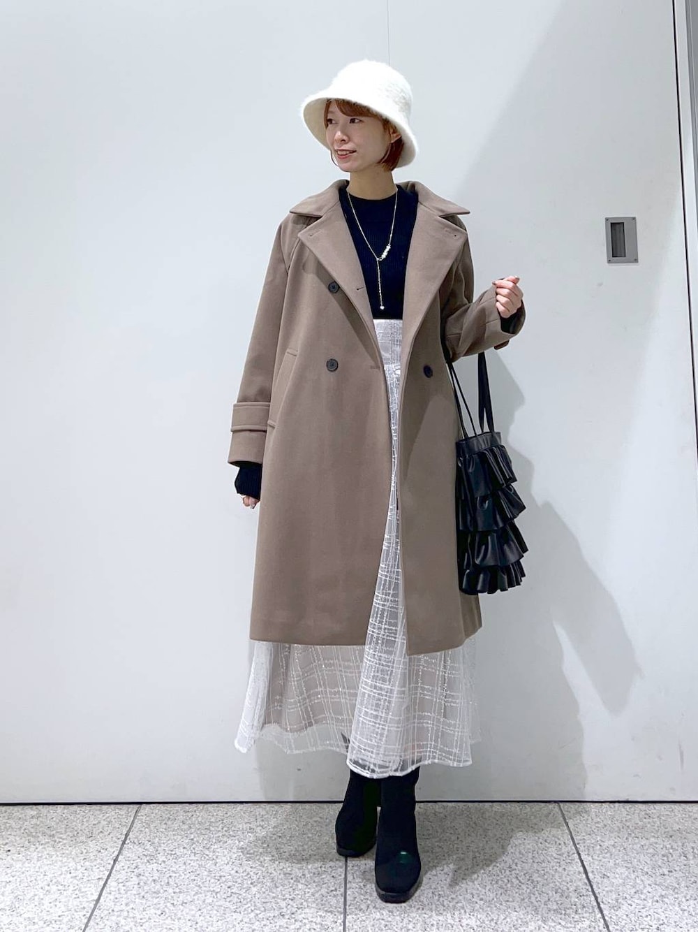 ブラウン系のチェスターコート、ブラック系のブーツ、ブラック系のニット/セーターを着用したレディースの冬コーディネートの1枚目の写真