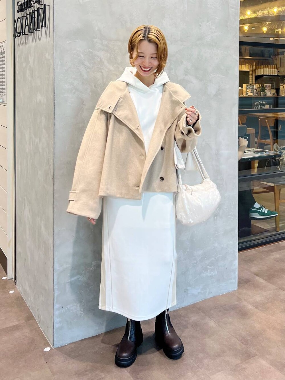 ベージュ系のピーコート、ホワイト系のショルダーバッグ、ブラウン系のブーツを着用したレディースの秋コーディネートの1枚目の写真