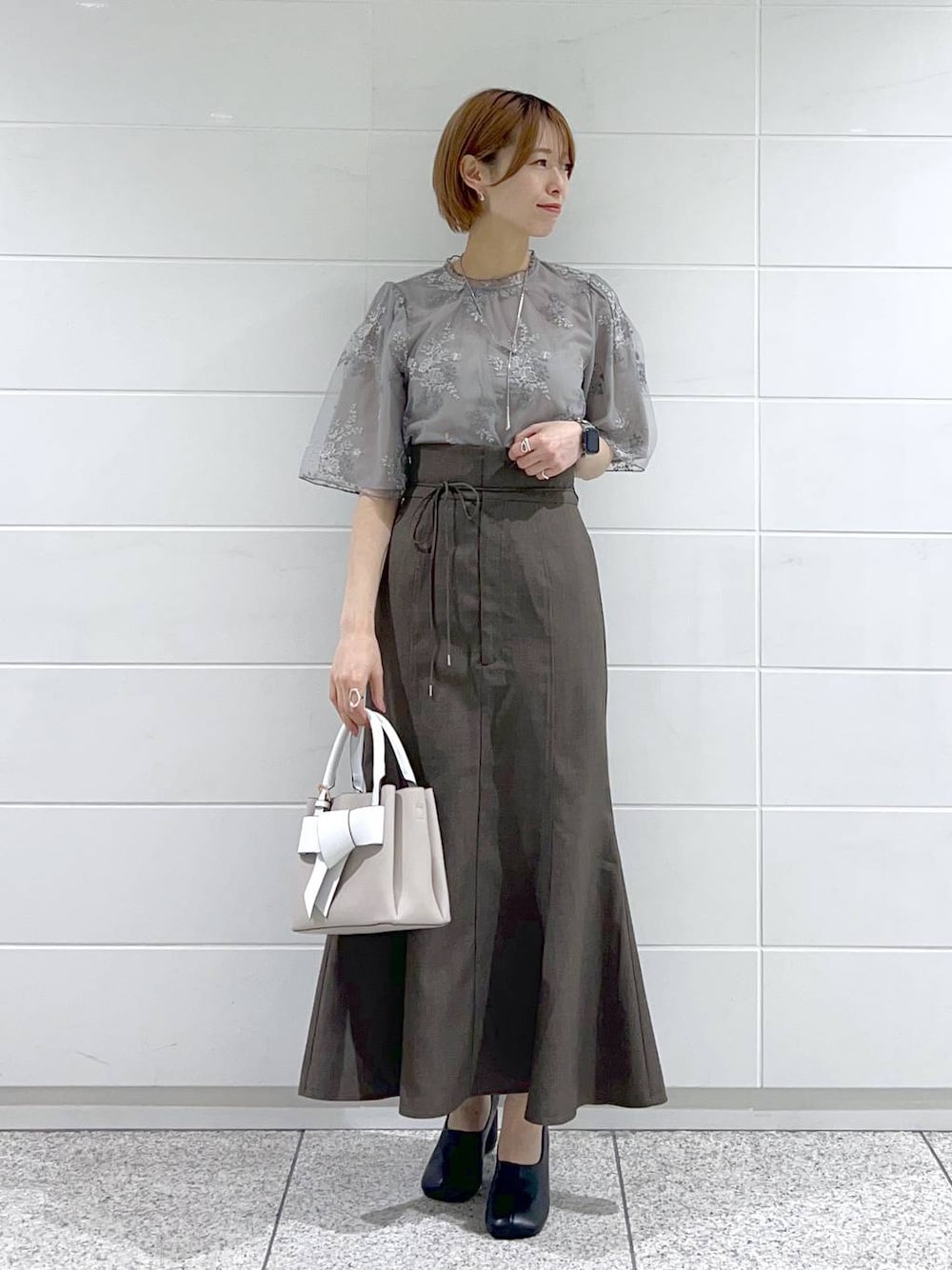 ベージュ系のショルダーバッグ、ブラック系のパンプス、グレー系のスカートを着用したレディースの春コーディネートの1枚目の写真
