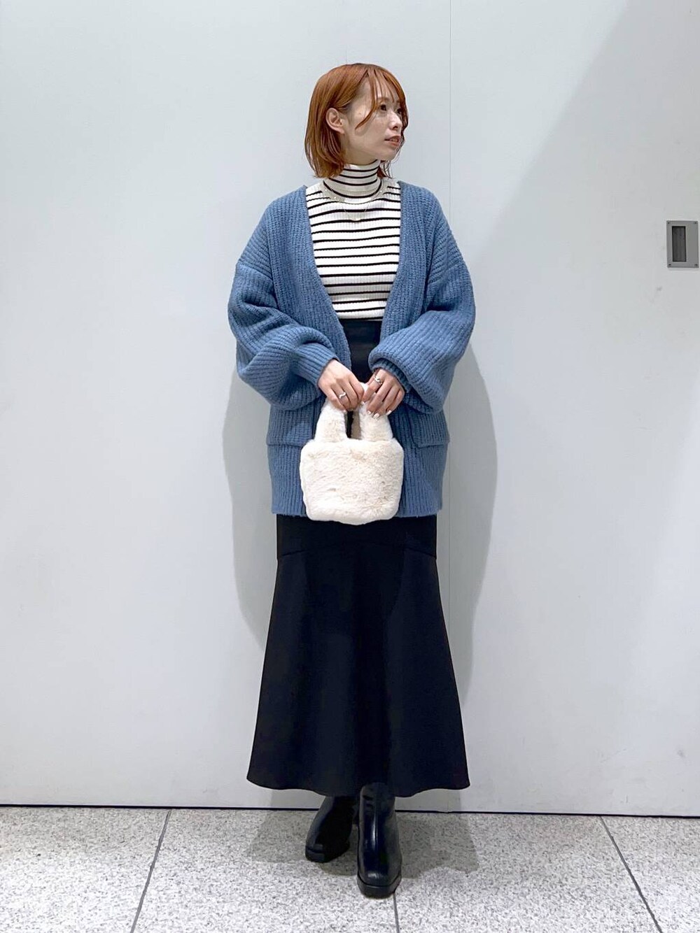 ブラック系のブーツ、ブラック系のスカート、ホワイト系のニット/セーターを着用したレディースの秋コーディネートの1枚目の写真