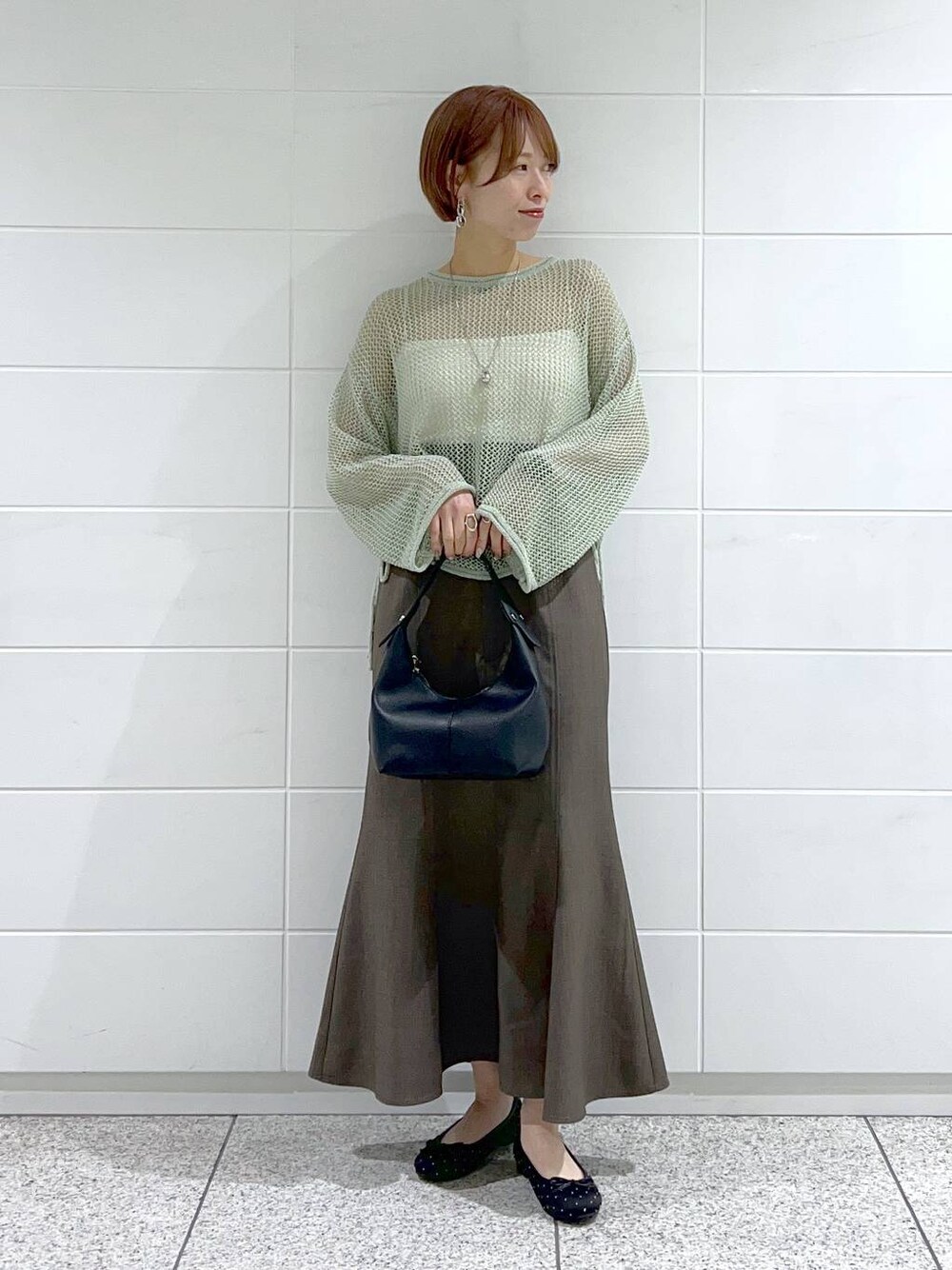 ブラック系のバレエシューズ、グリーン系のニット/セーター、グレー系のスカートを着用したレディースの春コーディネートの1枚目の写真