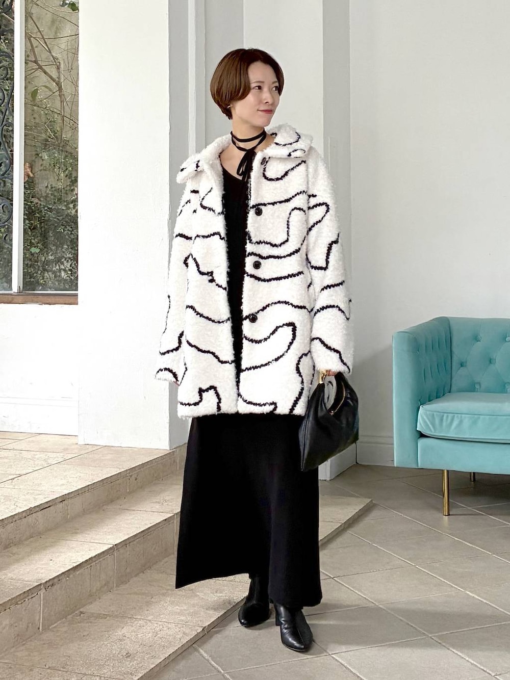 ブラック系のハンドバッグ、ホワイト系のステンカラーコート、ブラック系のブーツを着用したレディースの秋コーディネートの1枚目の写真