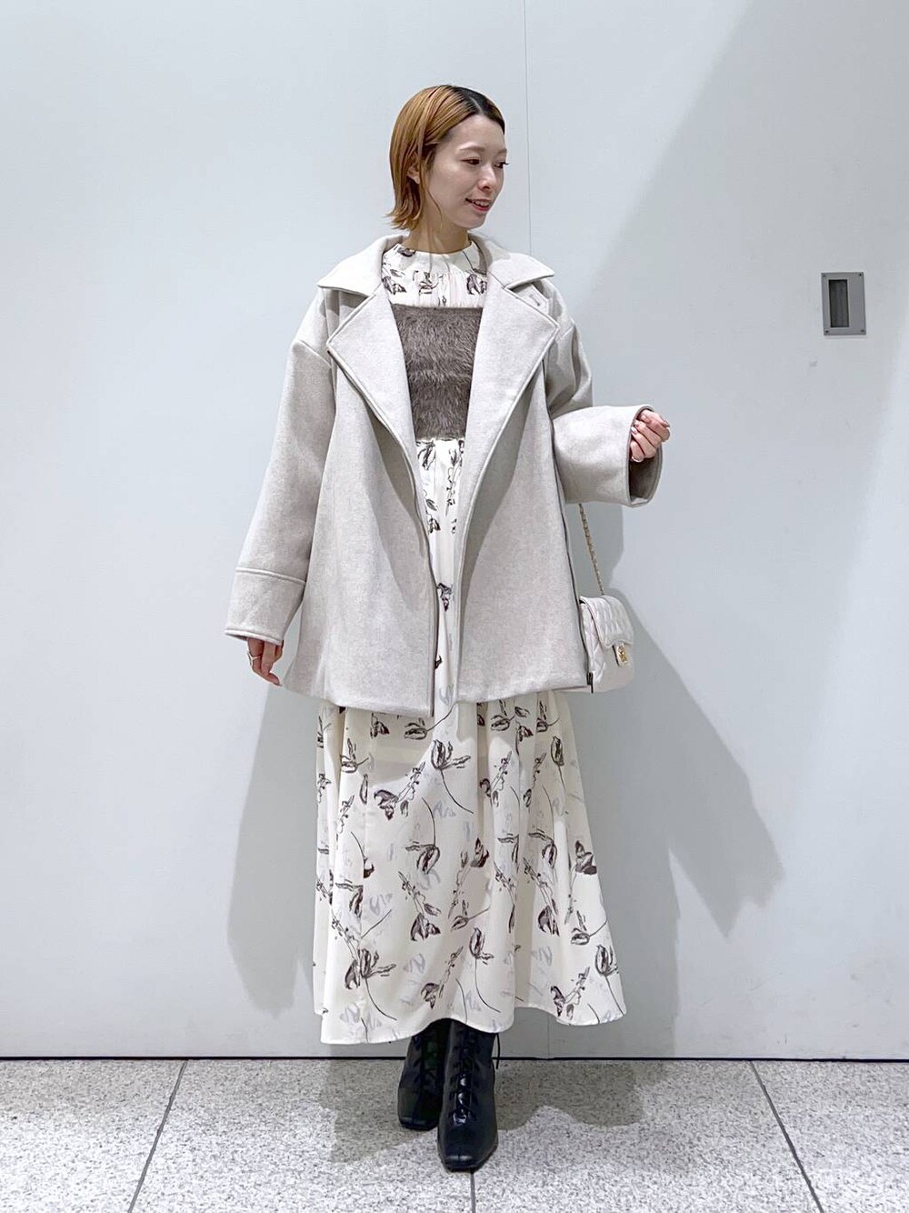 ホワイト系のショルダーバッグ、ブラック系のブーツ、ホワイト系のチェスターコートを着用したレディースの冬コーディネートの1枚目の写真