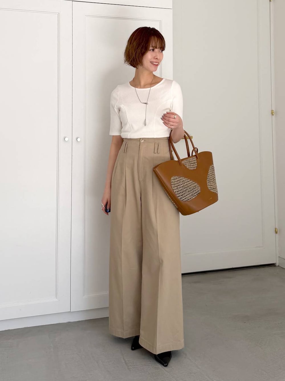 ブラウン系のトートバッグ、ブラック系のサンダル、ホワイト系のTシャツ/カットソーを着用したレディースの春コーディネートの1枚目の写真