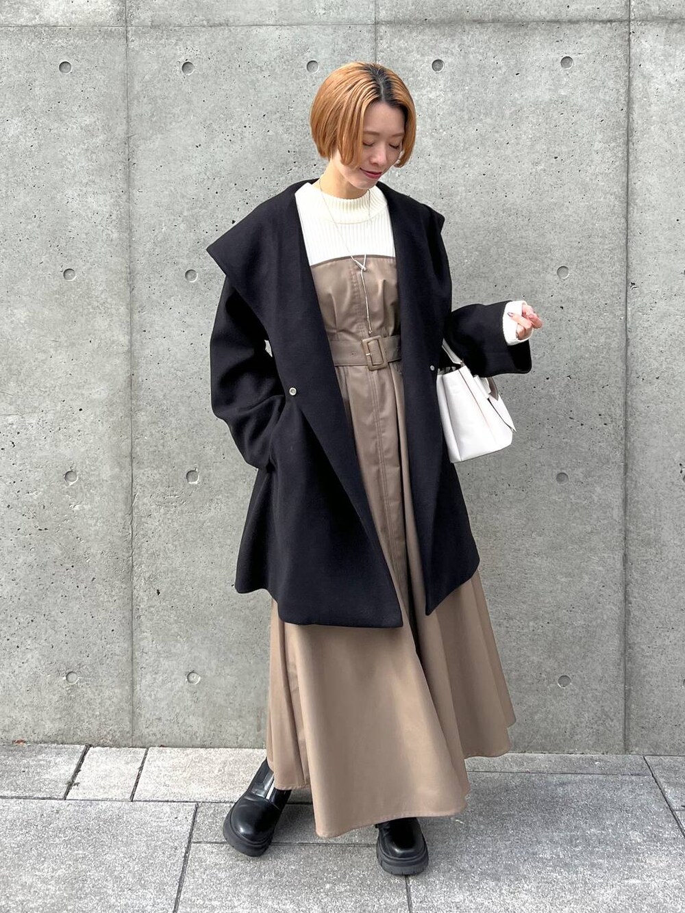 ブラック系のノーカラーコート、ブラック系のブーツ、ホワイト系のショルダーバッグを着用したレディースの冬コーディネートの1枚目の写真