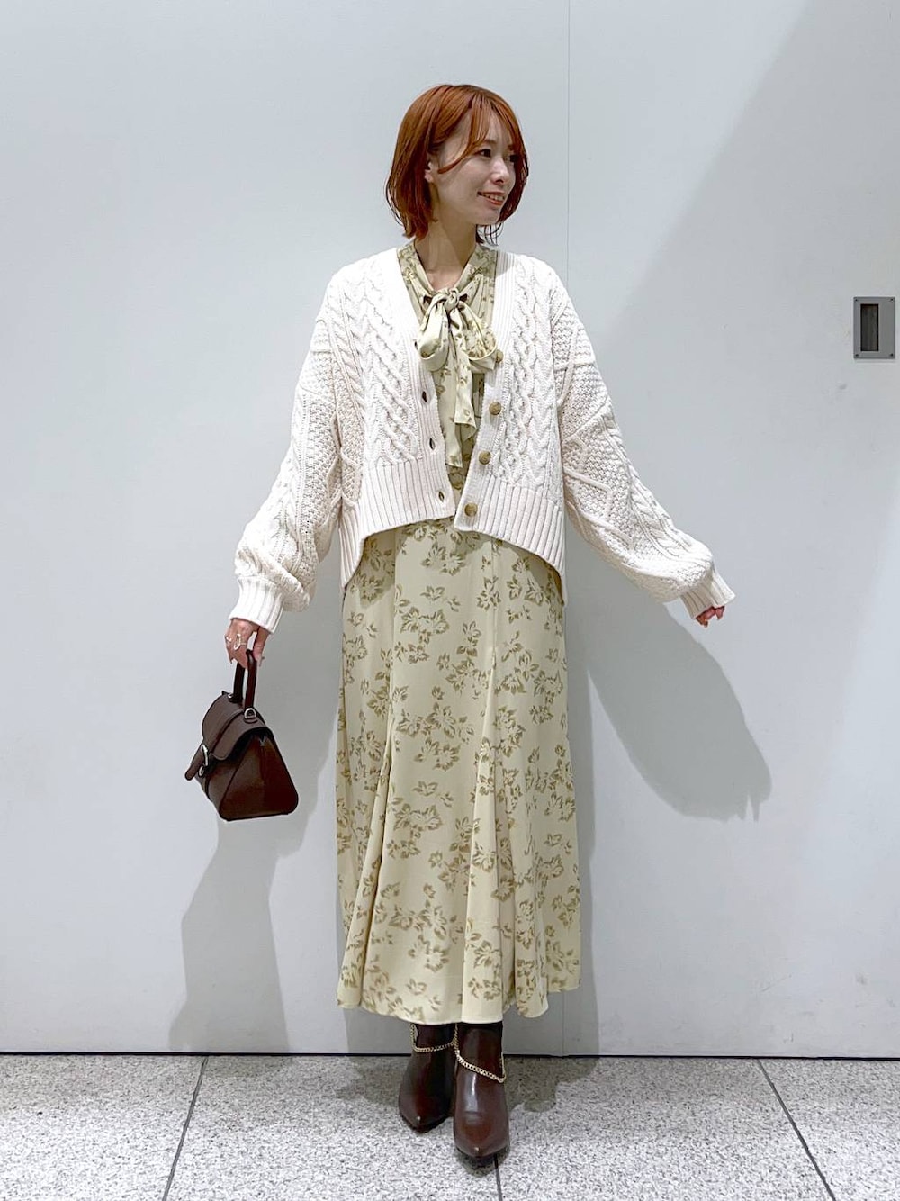 ブラウン系のハンドバッグ、ベージュ系のワンピース、ホワイト系のカーディガン/ボレロを着用したレディースの秋コーディネートの1枚目の写真