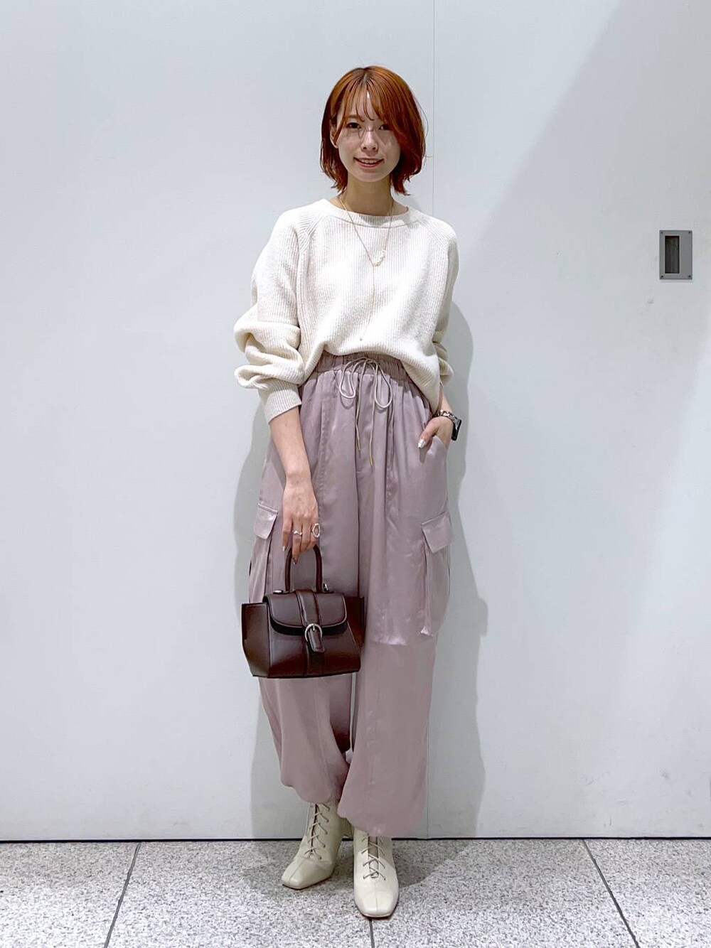 ホワイト系のニット/セーター、ブラウン系のハンドバッグ、ホワイト系のブーツを着用したレディースの秋コーディネートの1枚目の写真