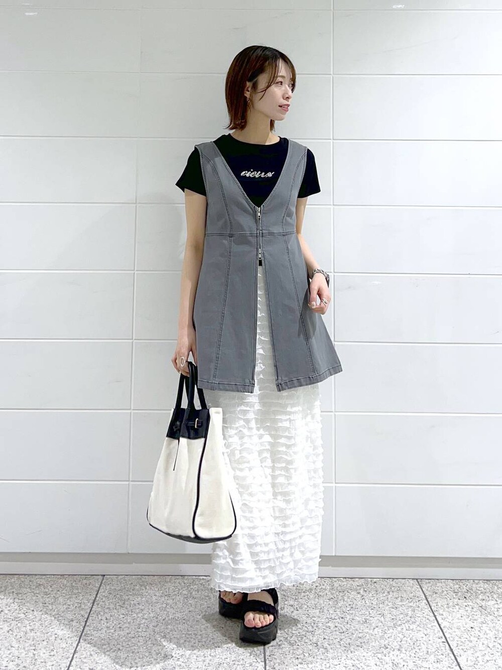 ブラック系のトートバッグ、ブラック系のTシャツ/カットソー、ブラック系のサンダルを着用したレディースの春コーディネートの1枚目の写真