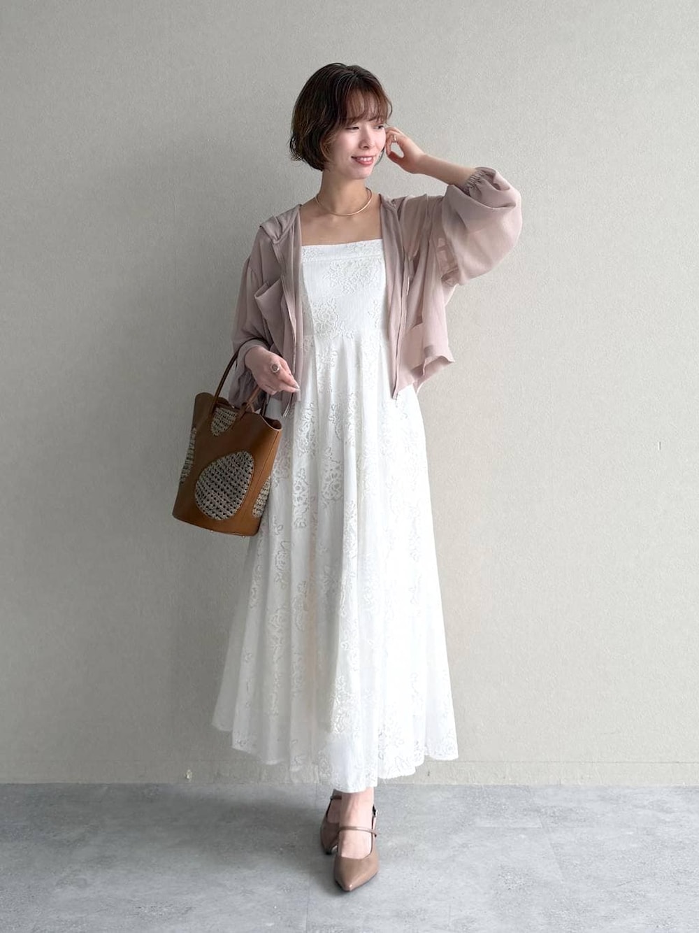 ベージュ系のパーカー、ブラウン系のトートバッグ、ホワイト系のワンピースを着用したレディースの春コーディネートの1枚目の写真