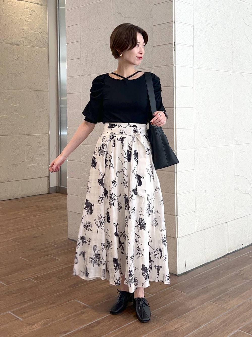 ブラック系のショルダーバッグ、ブラック系のTシャツ/カットソー、ホワイト系のスカートを着用したレディースの夏コーディネートの1枚目の写真