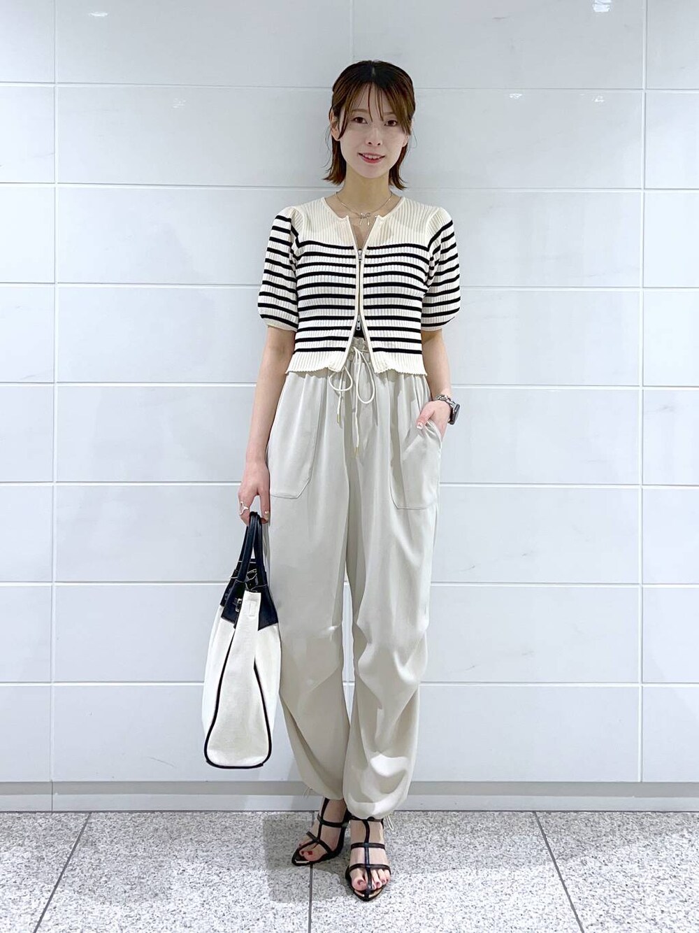 ブラック系のトートバッグ、ブラック系のサンダル、ホワイト系のベストを着用したレディースの春コーディネートの1枚目の写真